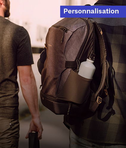 Un homme portant un sac à dos gris avec une gourde blanche dans la poche latérale, illustrant la personnalisation d'équipements de sport ou de voyage.