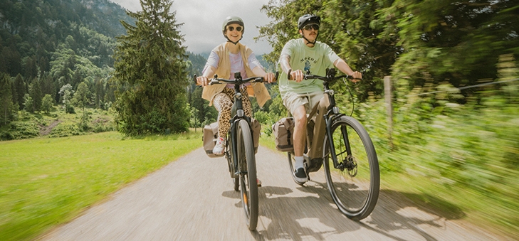 Un couple souriant à vélo sur un sentier en pleine nature.